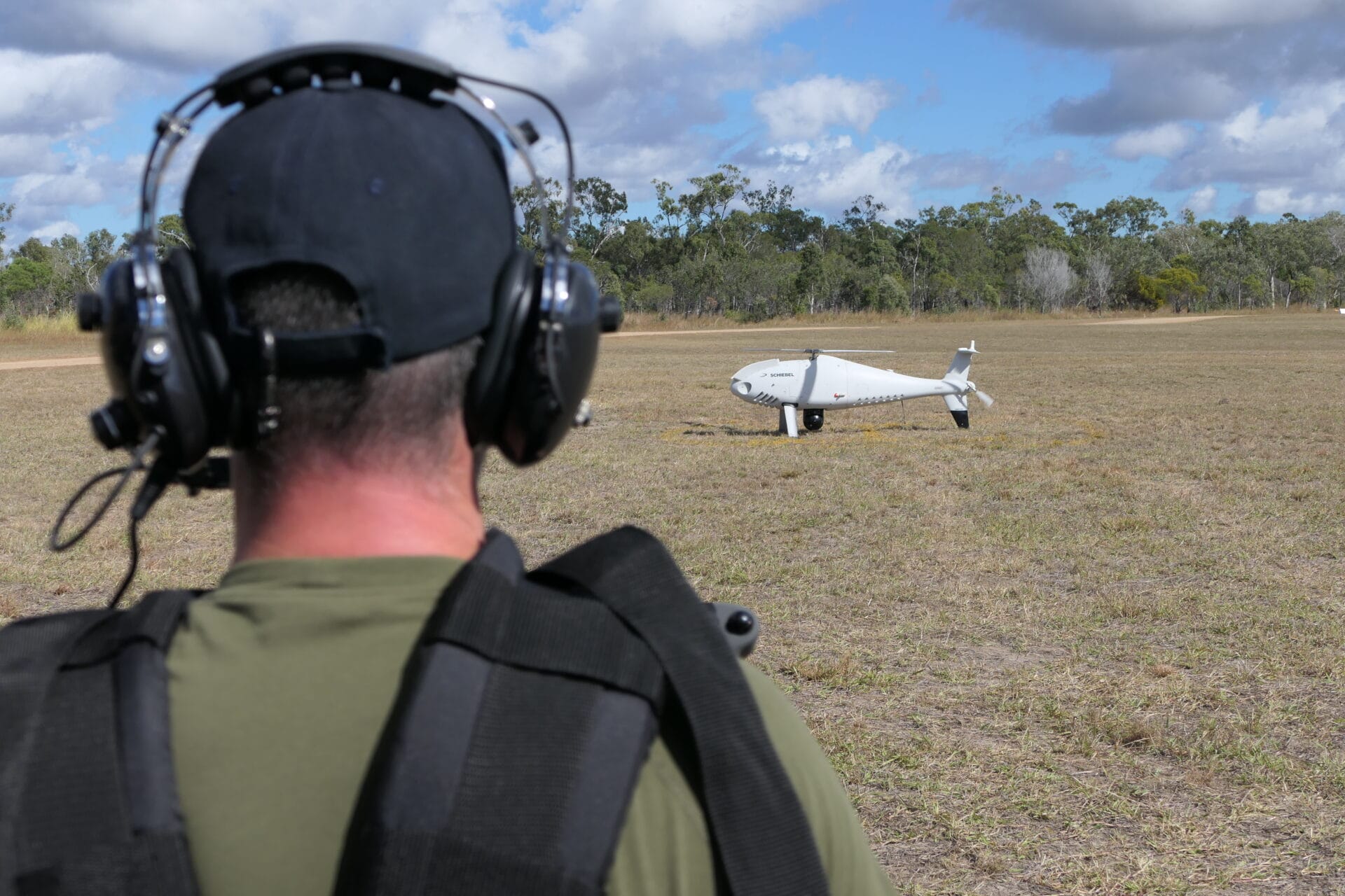 UAS operator back-on in the foreground with a Schiebel S-100 UAS on the ground in the background