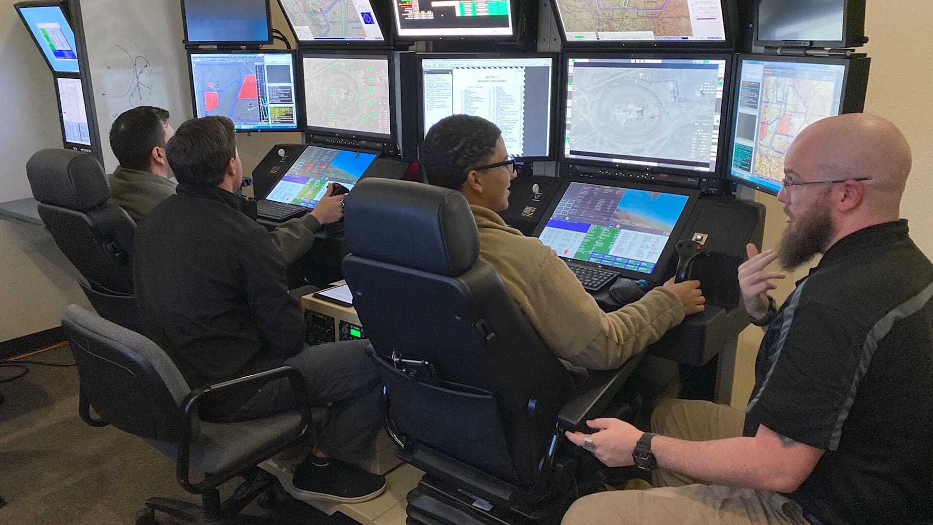 Photograph of a training session with 2 students and 2 instructors at the training consoles